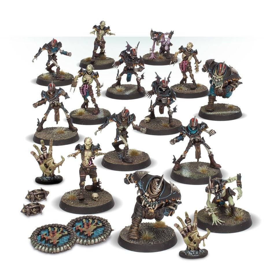 A group of painted Shambling Dead Blood Bowl miniatures on round textured bases, including skeletal and armored players in dark brown, teal and purple gear. Two blue circular markers, small footballs and skeletal-hand accessories are arranged alongside them.