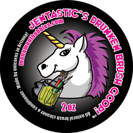 Circular black label graphic for brush cleaner, featuring a white unicorn with a purple mane and yellow horn holding brushes in a yellow-green jar. Pink-and-white lettering reads “JENTASTIC’S DRUNKEN BRUSH GOOP!” and “2 oz.”
