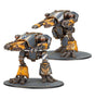 Two Warhound Scout Titan miniatures stand on round bases against a white background, shown from different angles. Both have slate-gray and ochre armor with metallic details, mounted weapons, and gold eagle emblems.
