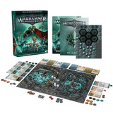 Warhammer Underworlds starter set displayed with its illustrated two-player box, rulebooks, token sheet, cards, dice and miniature figures. The dark teal and black hex-patterned game board is spread out below; the box reads “TWO-PLAYER STARTER SET.”