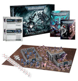 Warhammer 40,000 Ultimate Starter Set displayed with a box, rulebooks and reference sheets above blue armored Space Marine and pink-purple Tyranid miniatures arranged around gray terrain on a brown play mat, with dice and measuring rulers. The box reads “ULTIMATE STARTER SET.”