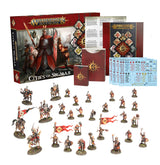 Cities of Sigmar army set arranged on a white background: a red illustrated Warhammer box, books and card sheets behind rows of small painted fantasy soldiers, mounted figures and red-and-gold banners. The box reads “WARHAMMER AGE OF SIGMAR” and “CITIES OF SIGMAR.”