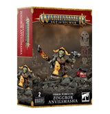 Box for two Orruk Warclans miniatures, showing a green-faced armored warrior with a flaming sword and a smaller red creature on rocky ground; the front and left side of the box are visible. Text reads “WARHAMMER AGE OF SIGMAR” and “ZOGGROK ANVILSMASHA.”