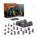 Kill Team: Nightmare tabletop game set on a white background, with an orange illustrated box and matching book behind a group of dark gray terrain pieces and two teams of painted miniatures on round bases. The box reads “KILL TEAM” and “NIGHTMARE.”