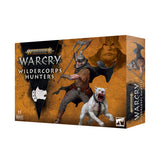 Warcry: Wildercorps Hunters game box shown from the front and right side, with orange-brown artwork of an armed hunter beside a snarling white dog. The front reads “WARHAMMER AGE OF SIGMAR,” “WARCRY,” “WILDERCORPS HUNTERS,” and “11 MINIATURES.”