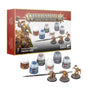 Warhammer Age of Sigmar Stormcast Eternals paint set shown with its red-and-white box, six paint pots, a brush and three gold-armored miniatures on round bases. The box reads “WARHAMMER AGE OF SIGMAR” and “STORMCAST ETERNALS PAINT SET.”