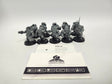Ten unpainted grey Hearthkyn Warriors miniatures on round black bases, posed with weapons and backpacks, arranged behind two white cards. The top card reads "HQN-24 Warhammer 40,000 Hearthkyn Warriors Leagues of Votann"; the lower card shows a die logo with "FRONTLINE GAMING CHAMPIONS OF TABLETOP".