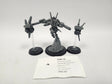 Unpainted gray assembled Warhammer 40,000 miniature set on three black round bases: a central armored figure on a sculpted rocky base flanked by two small drone units on clear flying stands. A label card in front reads "HQE-18", "Warhammer 40,000 Commander Shadowsun" and "Tau Empire".