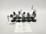 Group of unpainted gray plastic Age of Sigmar Grimghast Reaper miniatures on round black bases, hooded skeletal figures wielding scythes and polearms, with loose weapon parts on the table and a white label in front reading "HJZ-22 Age of Sigmar Grimghast Reapers" and "Nighthaunt".