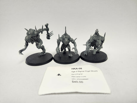 Three unpainted gray Crypt Ghoul miniatures on black oval bases, each crouching with claws and spikes, one raising a bone-like club; a white paper label in front reads "HKA-08" and "Age of Sigmar Crypt Ghouls".