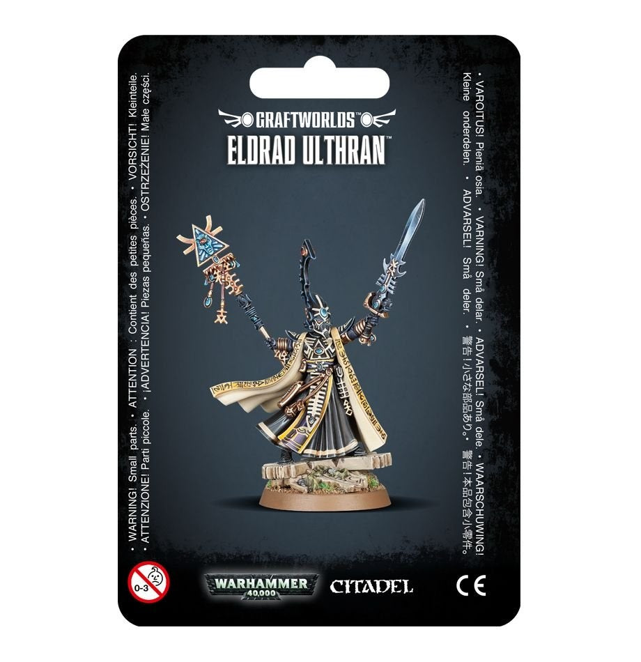 A packaged Eldrad Ulthran miniature stands on a rocky round base, wearing flowing cream-and-black robes with gold markings and raising a staff and sword. The black card reads “CRAFTWORLDS” and “ELDRAD ULTHRAN,” with Warhammer 40,000 and Citadel logos below.