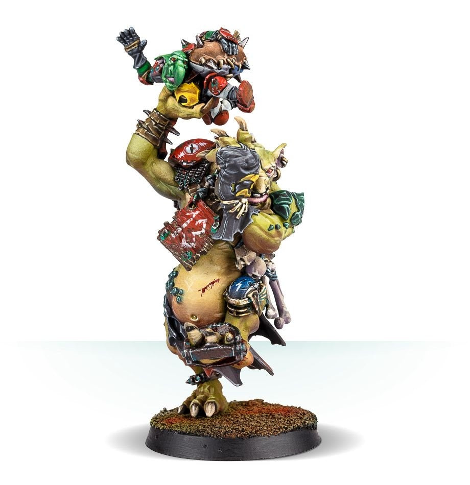 A painted Blood Bowl troll miniature stands on a round, dirt-textured base, carrying a smaller red-and-green armored player above its shoulders. The troll has green skin, a large belly, spiked armor and battered equipment.