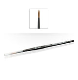 A slim black Citadel shade brush lies diagonally with a clear protective cap over one end and pointed brown bristles at the other. An inset shows the brush tip close up; the handle reads “SHADE” and “CITADEL.”