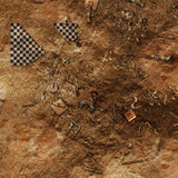 Top-down view of a square gaming mat printed with a rusty brown dirt-and-scrap terrain design, scattered with debris and small wreckage details. Two black-and-white checkered triangular markings sit near the upper-left corner.