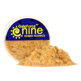 A clear round tub of tan, straw-colored static grass, with a loose pile spilling out in front. Its blue-and-yellow label reads “GaleForce nine” and “HOBBY SCENICS.”