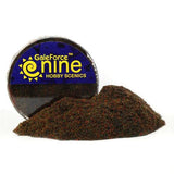 A mound of mottled dark brown, green, and rust-colored basing flock sits in front of a round container with a blue-and-yellow label reading “GaleForce nine” and “HOBBY SCENICS.”