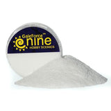 A small round clear container of white, fine-textured snow basing material is tipped forward, with a mound spilled in front. Its dark blue label reads “GaleForce nine” and “HOBBY SCIENCES” in yellow lettering.