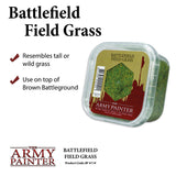 A clear plastic tub filled with mottled green and brown field grass flock, shown at an angle with a green label, red miniature-soldier silhouette and “THE ARMY PAINTER” logo. The package reads “BATTLEFIELD FIELD GRASS.”