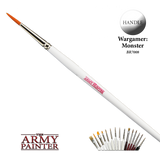 A large paintbrush runs diagonally across a black background, with orange pointed bristles, a shiny metal ferrule and a long white handle marked “ARMY PAINTER.” A “HANDLE” callout, The Army Painter logo and a row of smaller brushes appear below.