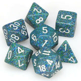 Seven blue-green speckled polyhedral dice with white numerals are grouped on a white background. The set includes several different shapes, including a cube, triangular-sided dice and a rounded-sided die.