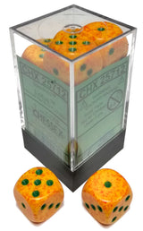 A clear square display case with a black base holds orange-yellow, red-speckled six-sided dice with dark green pips; two matching dice sit in front. The case label reads “CHESSEX”.
