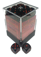 Opaque black six-sided dice with red pips are packed in a clear square display box, with two loose dice in front showing different faces. The red box label reads “CHX 25818” and “CHESSEX”.