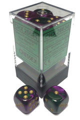 Two glossy six-sided dice with swirling green and purple coloring and gold pips sit in front of a clear display box with a dark base; more dice are visible inside. The box label prominently reads “CHESSEX.”