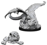 Unpainted gray Black Dragon Wyrmling miniature crouches on a round black base, with textured scales, curled tail and broad raised wings. A separate detailed skull with clustered stones sits below it.