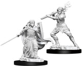 Two gray, unpainted fantasy paladin miniatures stand on black bases against a white background. One wears a flowing cloak and holds a sword and shield; the other crouches with a long-handled weapon across her shoulders.
