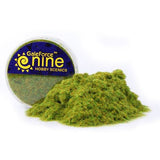A clear round tub of green static grass sits behind a loose mound of fine green fibers with yellow and brown flecks. Its blue-and-yellow label reads “GaleForce nine” and “HOBBY SCENICS.”