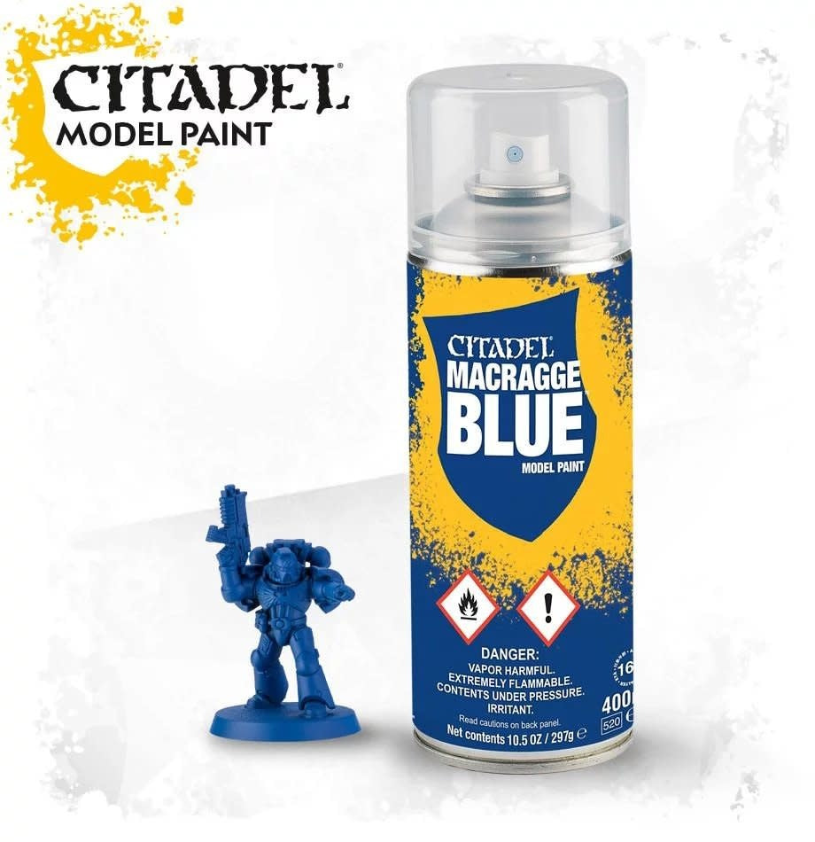 A yellow-and-blue Citadel spray can with a clear cap stands beside a small blue armored miniature holding a raised weapon. The label reads “CITADEL MACRAGGE BLUE” and “MODEL PAINT.”