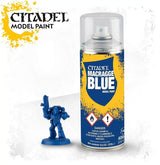 A yellow-and-blue Citadel spray can with a clear cap stands beside a small blue armored miniature holding a raised weapon. The label reads “CITADEL MACRAGGE BLUE” and “MODEL PAINT.”