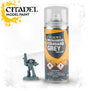 A yellow-orange spray can with a clear cap and black label stands beside a small grey miniature figure holding a raised weapon. The label reads “CITADEL MECHANICUS STANDARD GREY” and “MODEL PAINT”; “CITADEL MODEL PAINT” also appears at upper left.