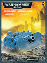 Front of a Space Marine Vindicator box featuring a large blue armored tank with a broad front cannon crossing rubble beneath a glowing yellow-orange city skyline. The package reads “WARHAMMER 40,000” and “SPACE MARINE VINDICATOR.”