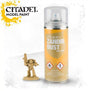 A yellow-orange Citadel Zandri Dust spray can with a clear plastic cap stands beside a small tan-painted armored miniature holding a raised weapon. The can reads “CITADEL,” “MODEL PAINT,” and “ZANDRI DUST.”