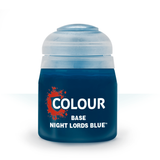 A squat, dark blue paint pot with a pale blue-gray domed lid is shown upright against a white background. Its label has a red paint-splatter graphic and the white text “COLOUR,” “BASE,” and “NIGHT LORDS BLUE.”