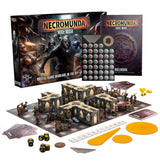 Necromunda: Hive War board game set displayed with its illustrated box and rulebook behind a laid-out battlefield of miniature figures, modular buildings and barricades, cards, tokens, dice, a measuring strip and orange templates. The box reads “NECROMUNDA” and “HIVE WAR.”