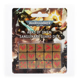 A blister pack displays fifteen gold-colored dice in a three-by-five grid, each marked with red winged emblems or pips, against illustrated armored warriors. The package reads “WARHAMMER 40,000” and “ARKS OF OMEN: SANGUINARY GUARD DICE.”