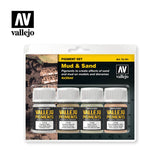 Vallejo “Mud & Sand” pigment set in a clear blister pack, with four small jars with white caps and labels in gray, brown, sienna and ochre tones. The black-and-yellow package also shows a muddy terrain scene and the “vallejo” logo.
