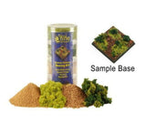 Summer Pasture basing kit shown with a clear cylindrical container behind piles of tan and brown grit and bright and dark green foliage. A square sample base covered in matching textures appears above the label “Sample Base.”