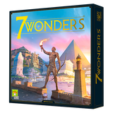 The front of the 7 Wonders board game box shows a man holding a flaming torch above an ancient city, with pyramids, towers and temples beneath a blue and pink sky. Large yellow lettering reads “7 WONDERS.”