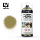 Vallejo Hobby Paint aerosol can with a clear cap and olive-yellow nozzle, shown beside a matching olive-yellow spray swatch on white. The label reads “vallejo” and “HOBBY PAINT,” with small model illustrations and hazard symbols.