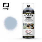 Vallejo Wolf Grey hobby paint primer aerosol can with a clear cap and black-and-white label, shown beside a pale blue-grey spray swatch. The label prominently reads “vallejo” and “HOBBY PAINT.”
