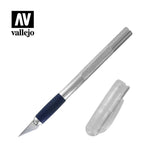 A silver craft knife with a pointed blade, dark navy grip and textured metal handle lies diagonally beside its clear plastic cap. The upper-left corner shows the black-and-white “AV” logo above the word “vallejo.”