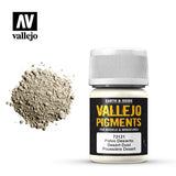 A white-capped bottle of Vallejo Desert Dust pigment stands beside a mound of pale beige powder. Its black label reads “VALLEJO PIGMENTS” and “Desert Dust,” with the Vallejo logo above.