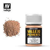 A small bottle of tan-brown Vallejo pigment with a white ribbed cap sits beside a loose mound of matching powder. The black label reads “VALLEJO PIGMENTS” and “New Rust.”