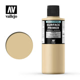 A beige Desert Tan primer bottle with a black cap and black label stands beside a round swatch of the matching tan color. The label reads “SURFACE PRIMER” and “Desert Tan,” with the “vallejo” logo above.
