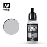A small gray primer bottle with a black ribbed dropper cap stands beside a round gray color swatch. Its black label reads “SURFACE PRIMER,” “70.601,” and “Grey,” with the Vallejo logo above.
