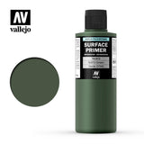 A dark olive-green Vallejo primer bottle with a black ribbed cap stands beside a matching round color swatch on white. The label reads “SURFACE PRIMER” and “NATO Green,” with a Vallejo logo.
