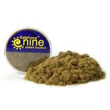 A loose mound of brown and olive dead static grass sits in front of a round clear tub with a blue-and-yellow label reading “GaleForce nine” and “HOBBY SCENICS.”